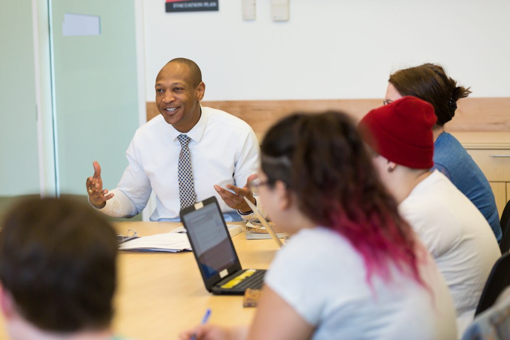 Richard Sévère, Ph.D., interim associate dean of Valpo's College of Arts and Sciences and professor of English, sitting at the head of a table of students as he lectures in a classroom on campus.