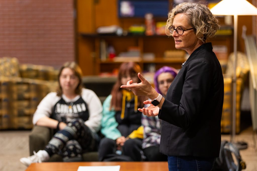 Jennifer Prough ’91, Ph.D., dean of Valpo's Christ College – The Honors College and professor of humanities and East Asian studies, standing and motioning with her hands as she lectures a small group of students in the furnished Mueller Hall commons on campus.