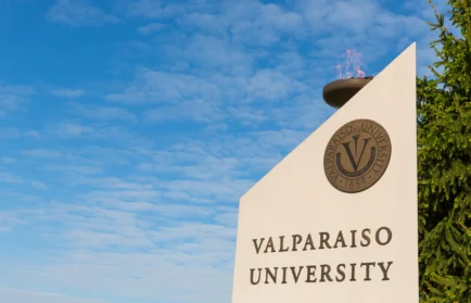 Valparaiso University sign with emblem and flame, set against a blue sky with some clouds, highlighting the university’s excellence that draws national attention.
