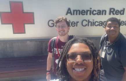 Three people smiling in front of an American Red Cross Greater Chicago sign on a sunny day, highlighting a memorable moment from a CAPS Fellow Story.
