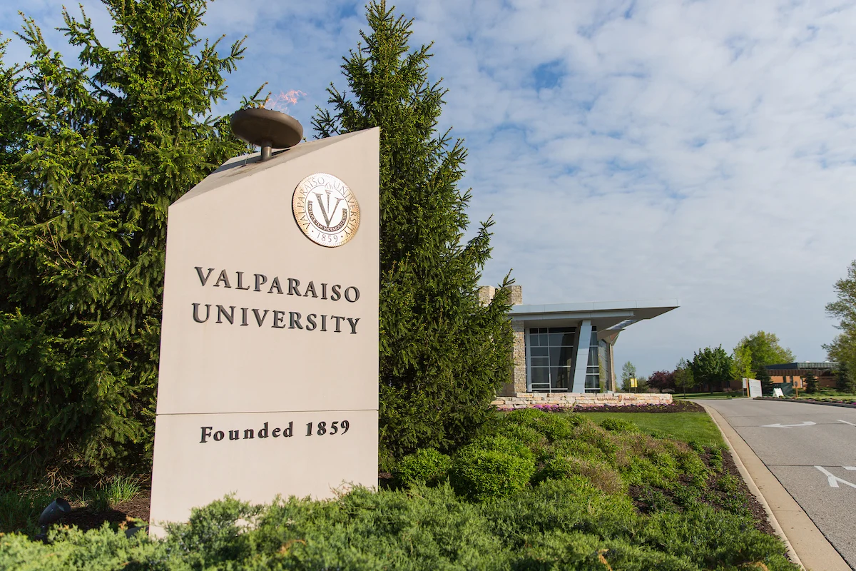 Valparaiso University entrance sign with campus building and greenery in the background.
