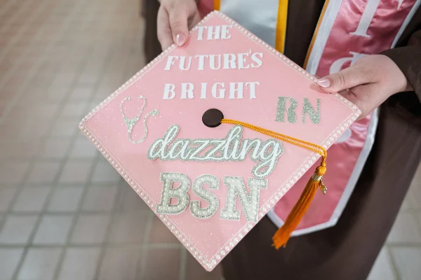 A pink graduation cap with sparkly letters reading “The Future’s Bright dazzling BSN RN” and a stethoscope design.