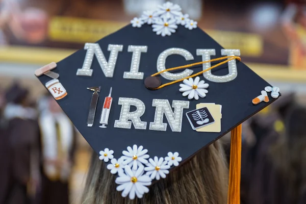 Graduation cap decorated with letters “NICU RN,” daisies, a syringe, x-ray image, and a medicine bottle.