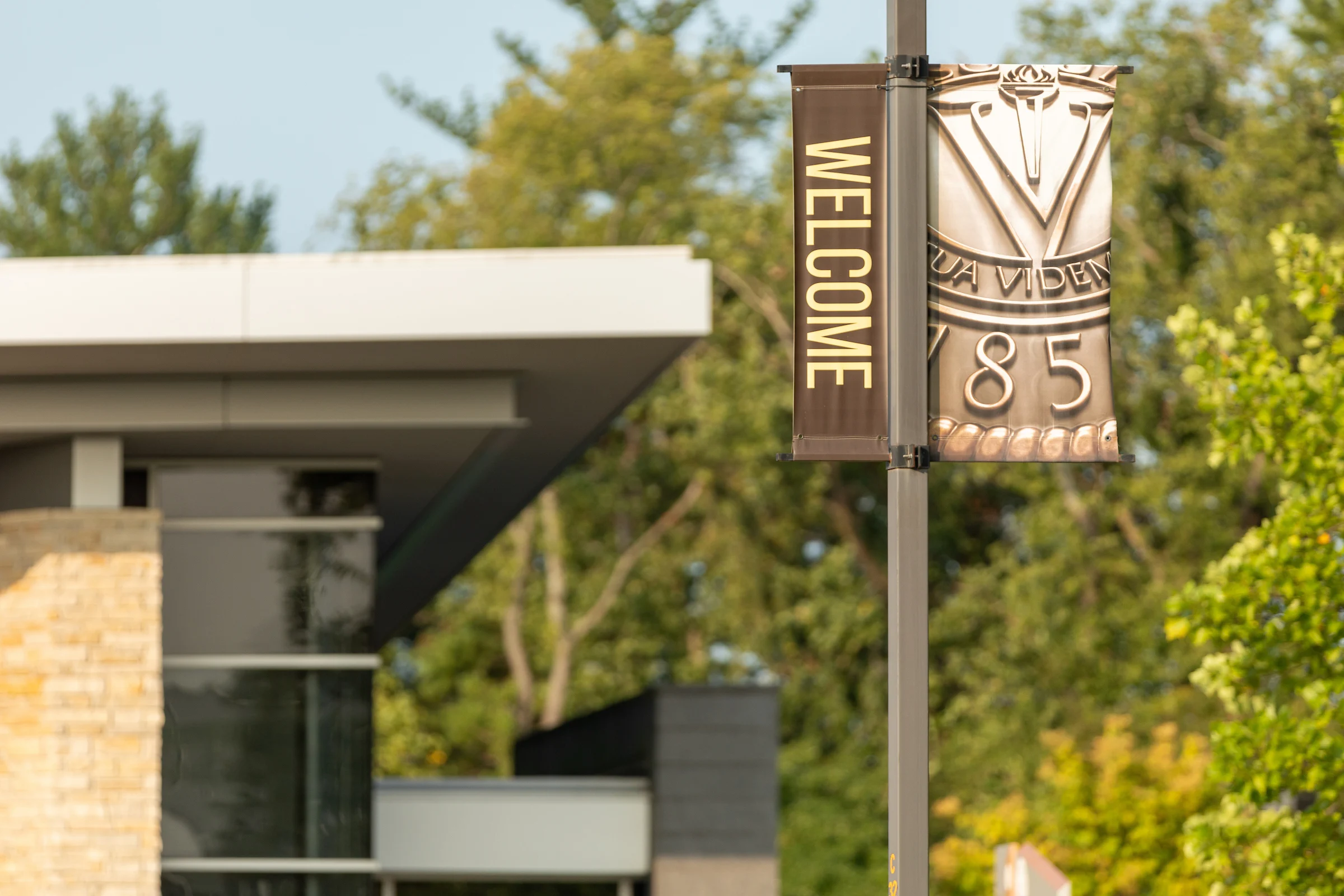 A “Welcome” banner hangs near a modern building and green trees.