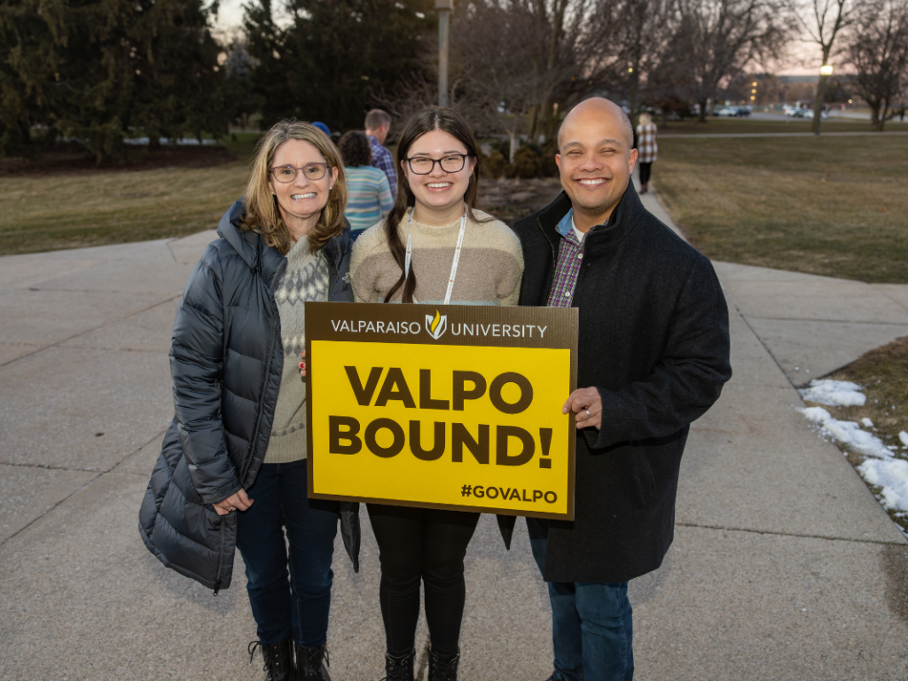 An admitted student poses with her parents and a Valpo Bound sign in front of Mueller Hall.