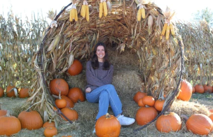 Nora Fisher sits on hay bales in a pumpkin patch, surrounded by pumpkins and corn stalks, capturing the warmth of autumn and the spirit of her Valpo experience at Valparaiso University.