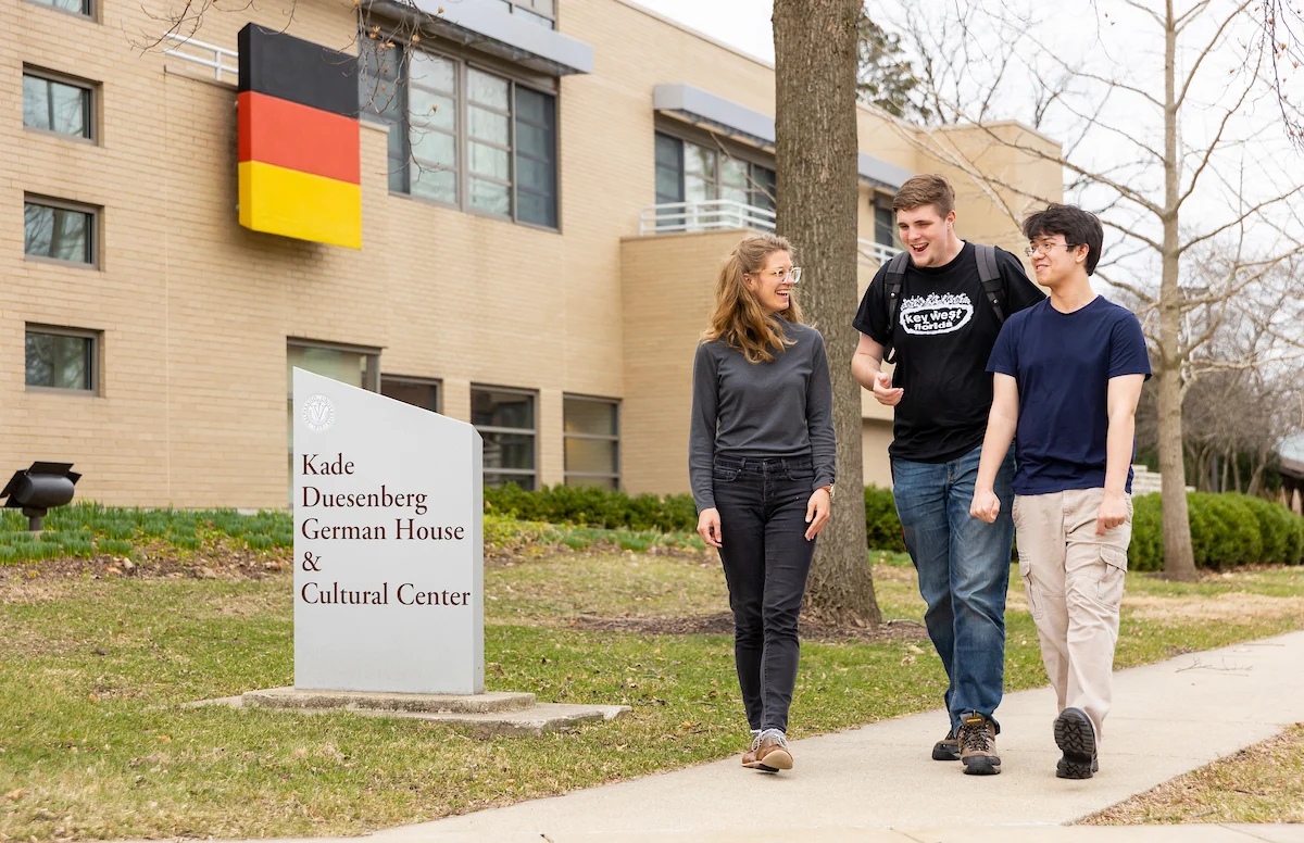 Three student profiles come to life as they walk and talk outside the Kade Duesenberg German House & Cultural Center on a college campus.