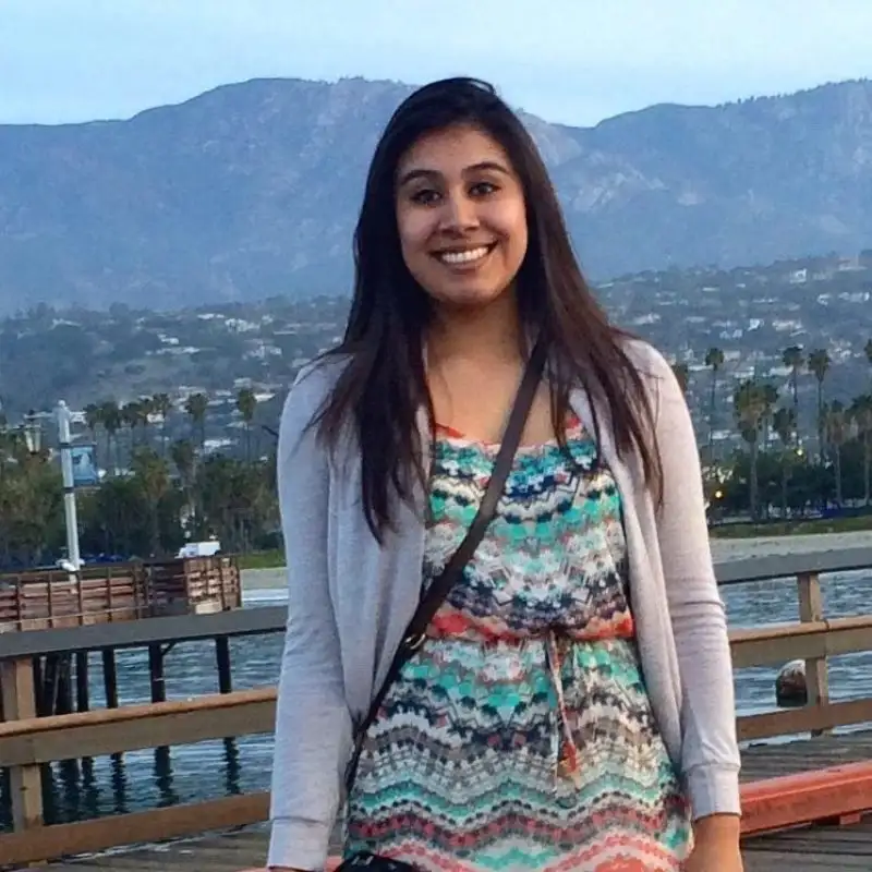 Woman in a colorful dress smiling on a pier, with mountains and water in the background—perfect for vibrant student profiles.