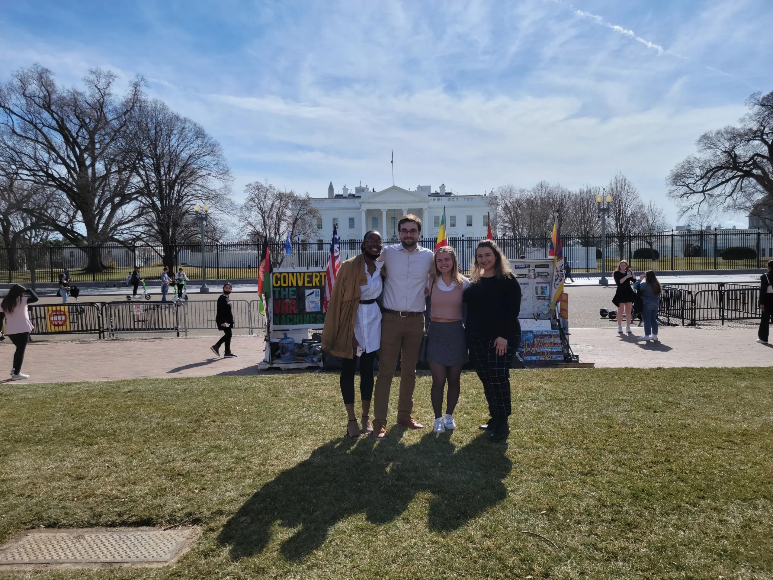 Four people pose together on the lawn in front of the White House on a sunny day, celebrating their internships.