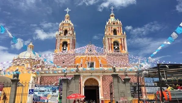 A bright yellow church with two domed towers, festive banners, and a blue sky with scattered clouds.