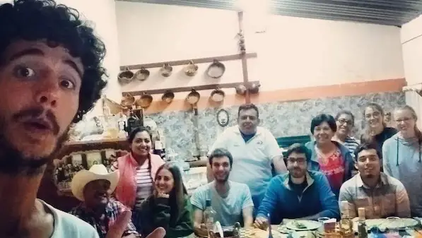 A group of people smiling and posing for a selfie around a dinner table in a cozy kitchen.