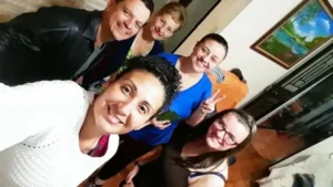 Five people smiling and posing for a selfie indoors, with a painting and open door in the background—capturing candid moments for their Student Profiles.
