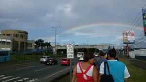 People walk along a busy street under a rainbow, with buildings, cars, and vibrant student profiles adding color to the lively background.