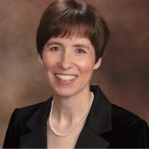 Woman with short brown hair, wearing a black suit and pearl necklace, smiling at the camera—an accomplished member of the Music Department.