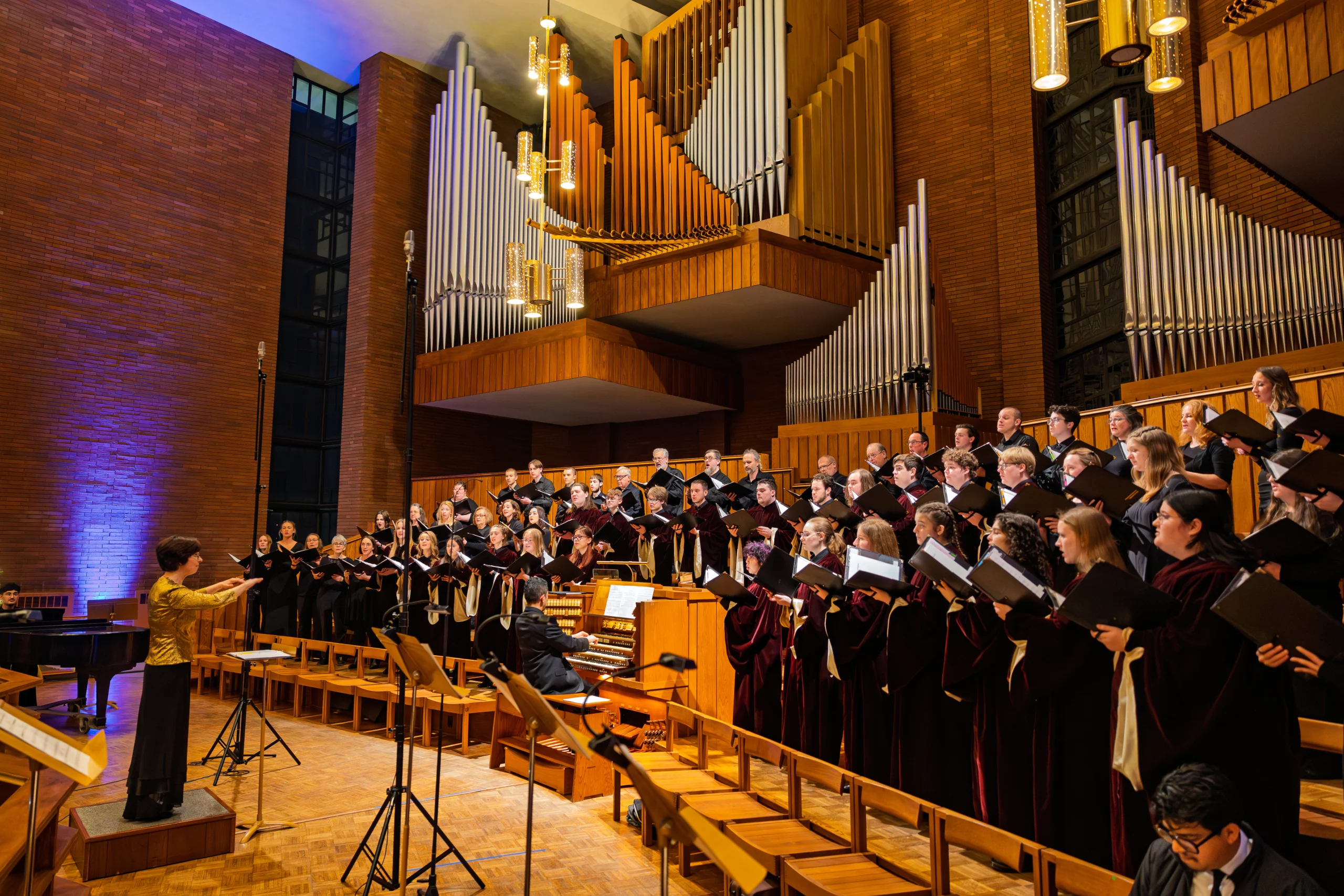 A choir from the Music Department performs in a church with a large pipe organ, directed by a conductor in front.