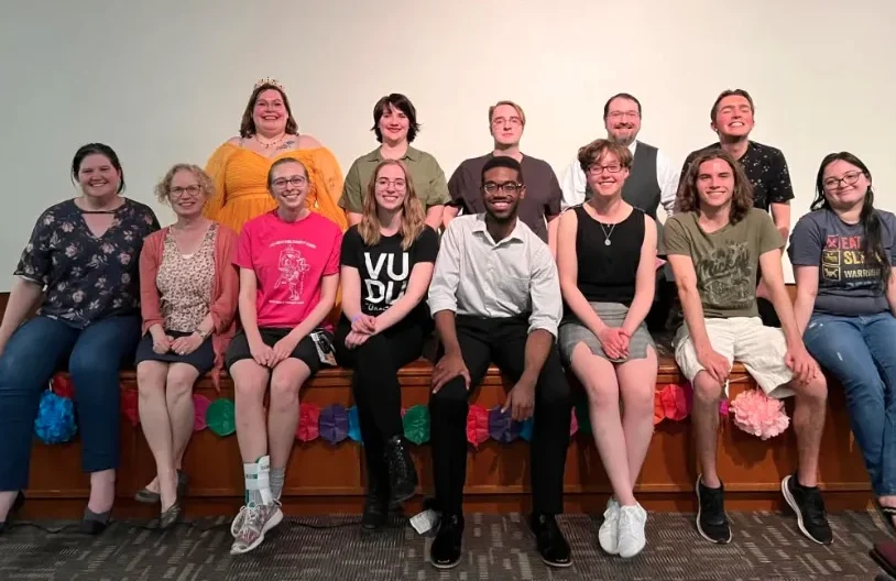 Thirteen people from student organizations pose together indoors, smiling, seated and standing in two rows against a plain background.