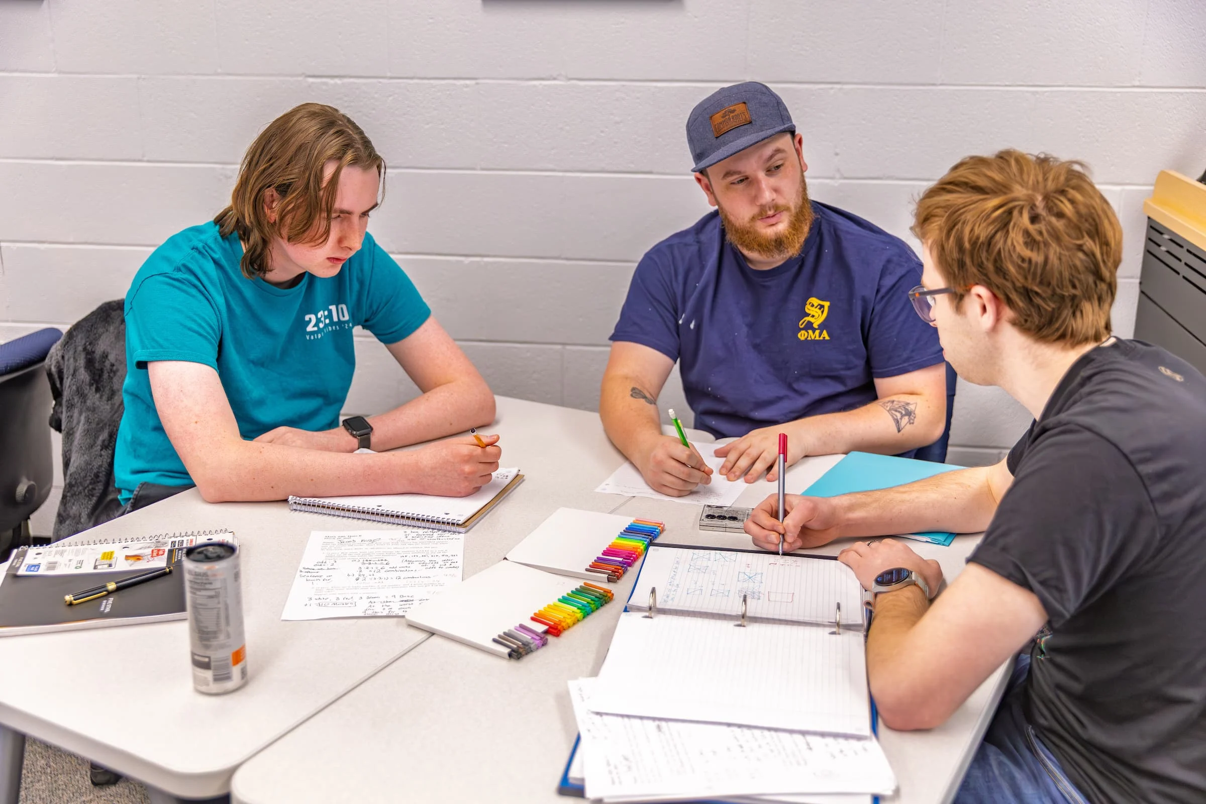 Three students sit at a table studying, writing in notebooks and using colored markers, making the most of the available Academic Resources.