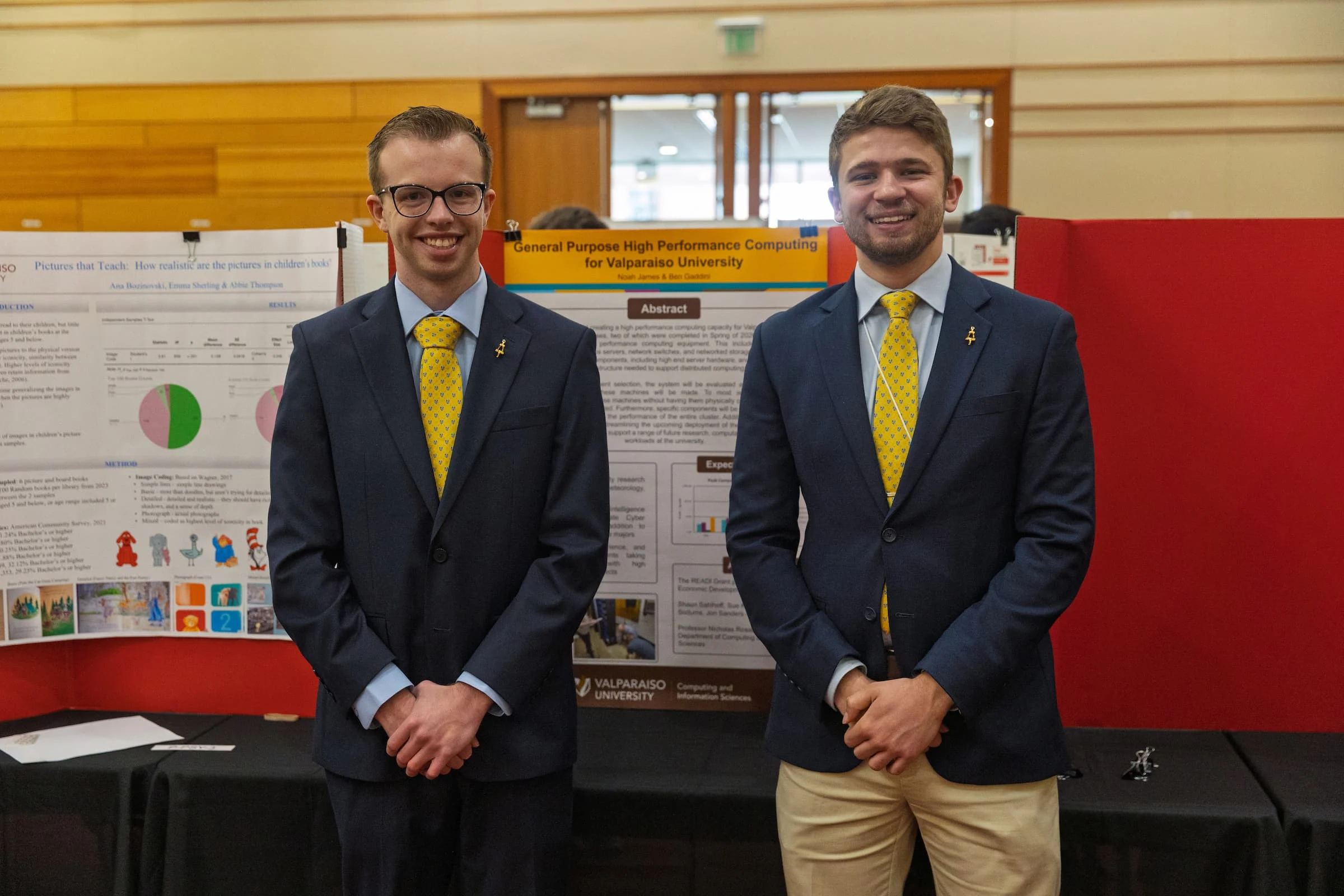 Two men in suits and yellow ties stand smiling in front of a science poster presentation in a conference room, showcasing their DEV project and commitment to experiential learning.