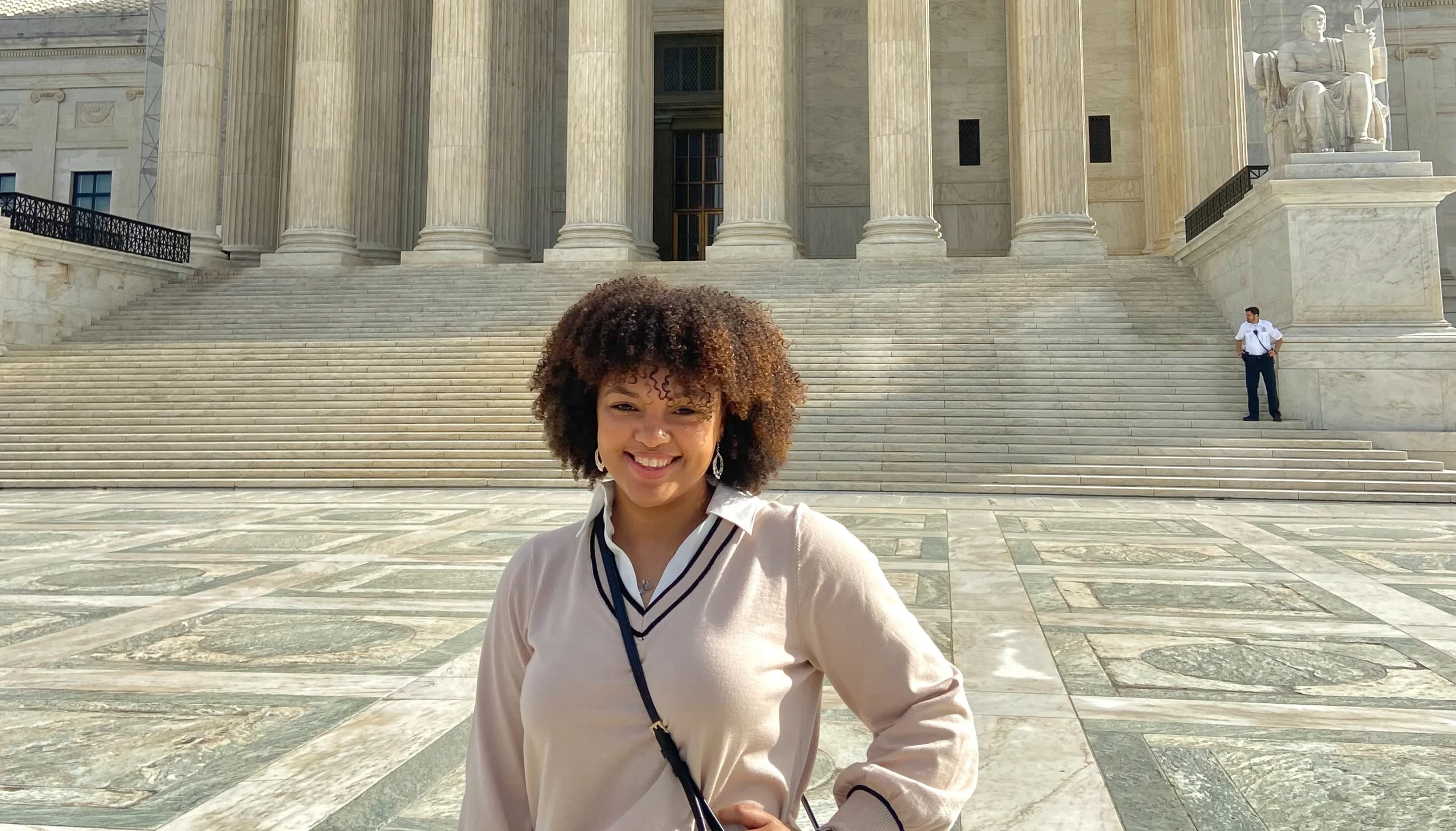Smiling person stands in front of a large stone building with columns and wide steps on a sunny day, embodying the spirit of experiential learning at this historic campus.