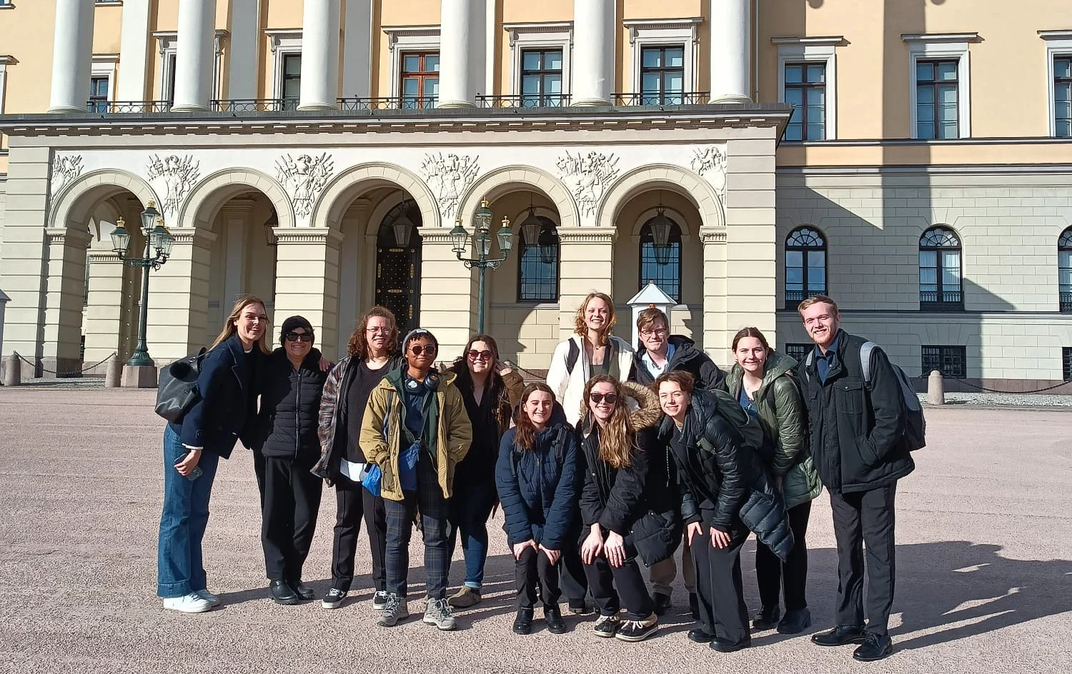 A group of people posing and smiling outside a large, ornate building on a sunny day, celebrating new Study Abroad opportunities.