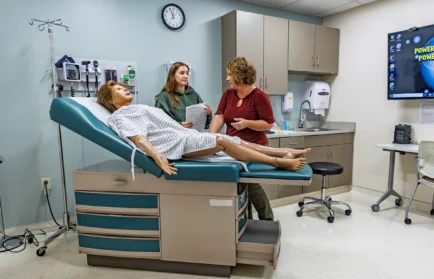 A nursing student discusses training with an instructor by a medical mannequin in a Valparaiso University program.