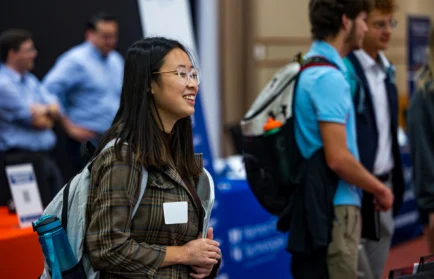A smiling young woman in a plaid jacket and name tag attends a career guidance event.