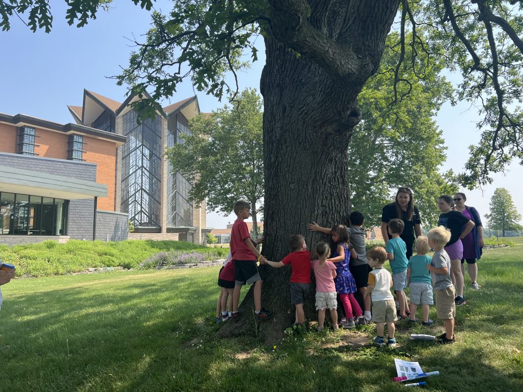 Children gather around the Merlin tree on campus
