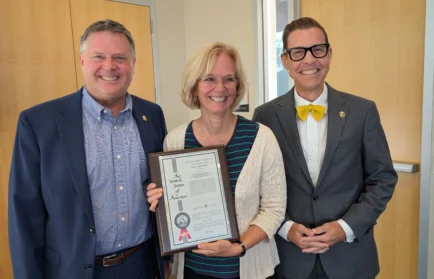 Three people smiling, with the center person holding a Valparaiso University patent for water filtration.