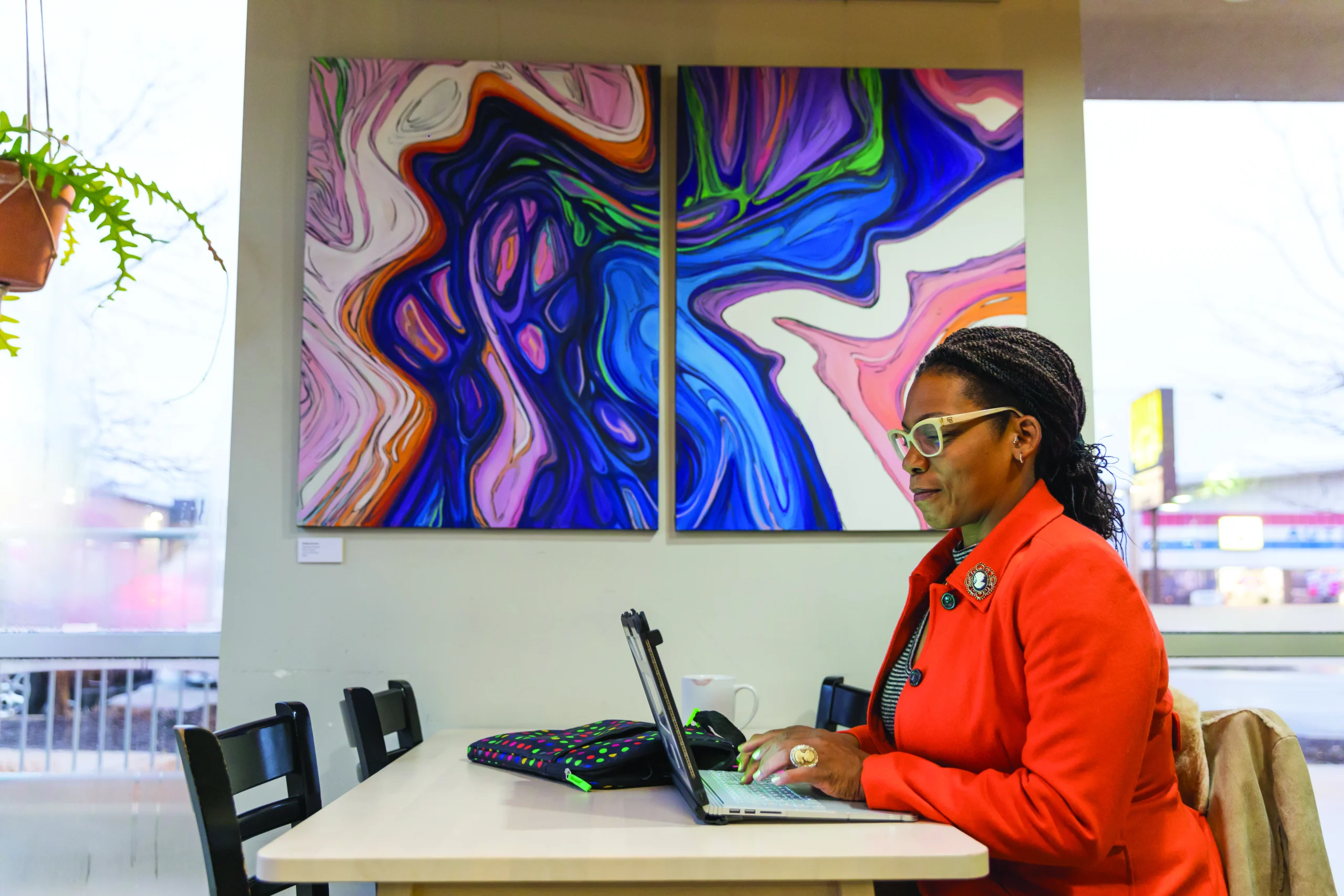A Valparaiso University graduate student works on online coursework on a laptop, seated at a table with colorful artwork behind her.