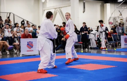 Two karate athletes spar in a competition, watched by an audience and officials in a gymnasium setting, as Valpo’s own World Champion Hailey Reichelt showcases her impressive skills.