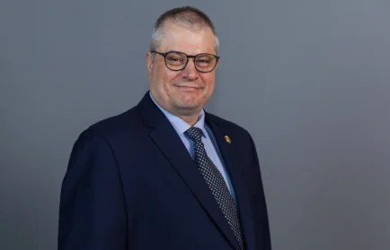 Man in a navy suit and glasses smiling, standing against a plain gray background. He is the Program Director for the Master of Organizational Leadership at Valparaiso University.