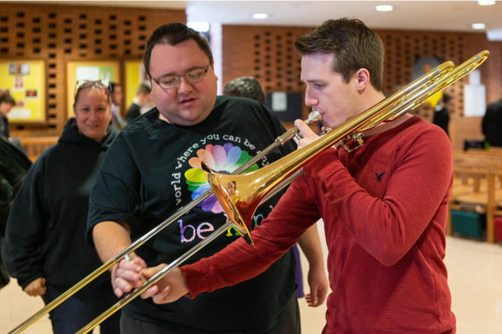 One male assisting another who is playing trombone