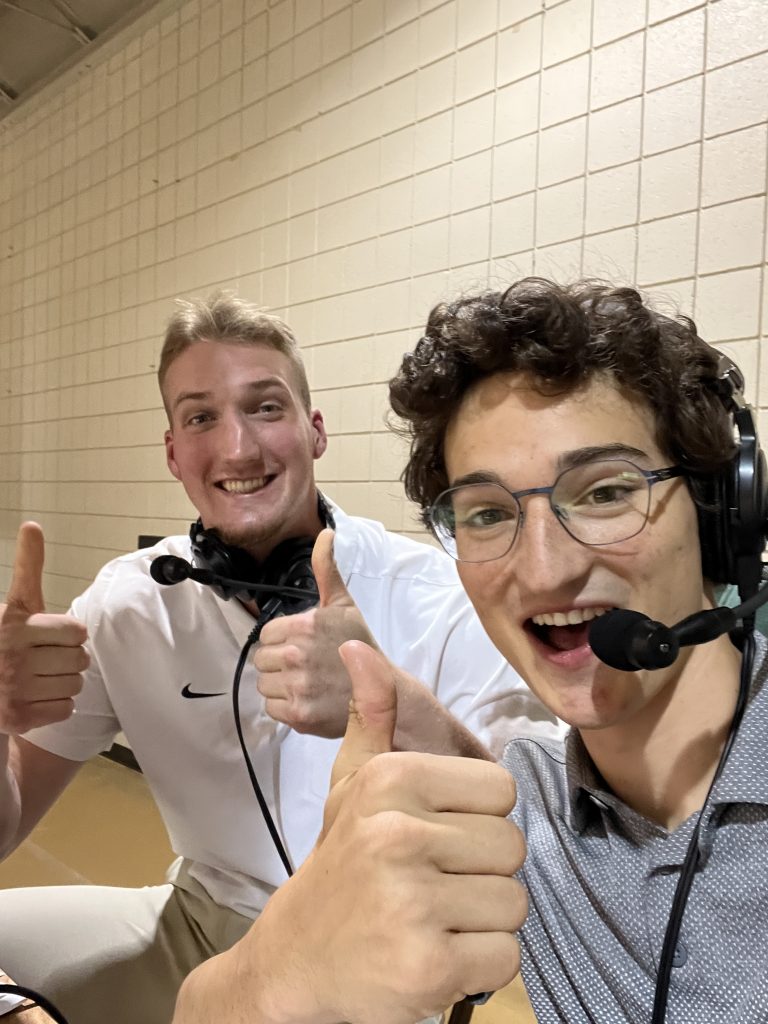 Noah Godsell '24 giving a thumbs up to the camera with a fellow WVUR-FM student at their station during a Valpo Athletics sporting event in the Athletics-Recreation Center (ARC).