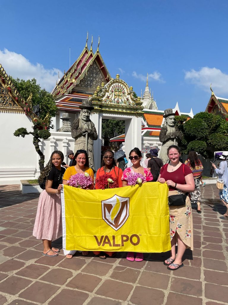 Valpo students posing in front of Thai monument in Thailand holding Valpo flag.