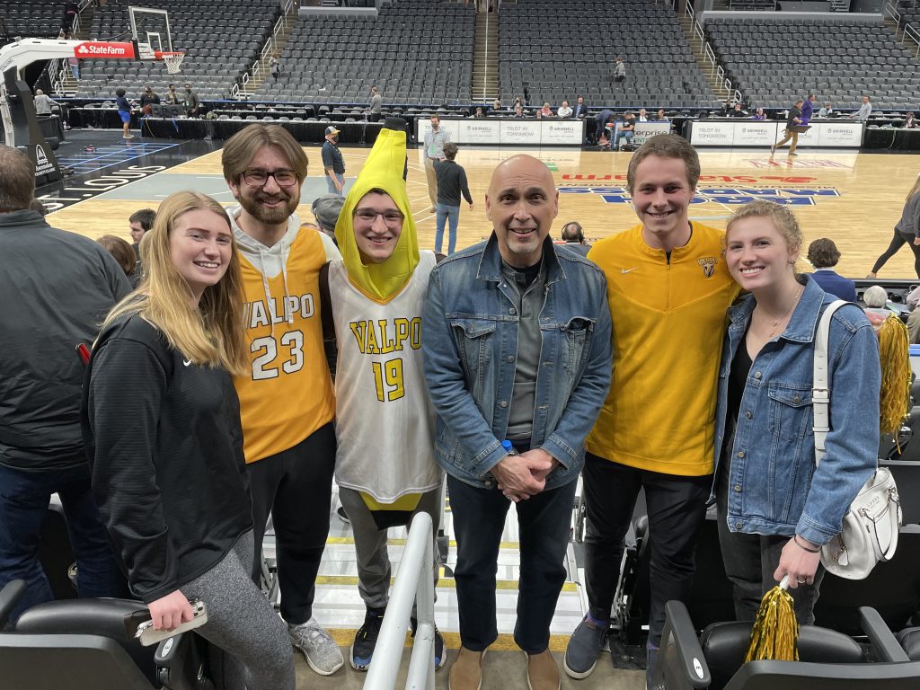 Noah Godsell '24 wearing Valpo merch over a banana costume alongside other Valpo students, staff members, and President José Padilla, J.D., in the Athletics-Recreation Center (ARC) after a men's basketball game.