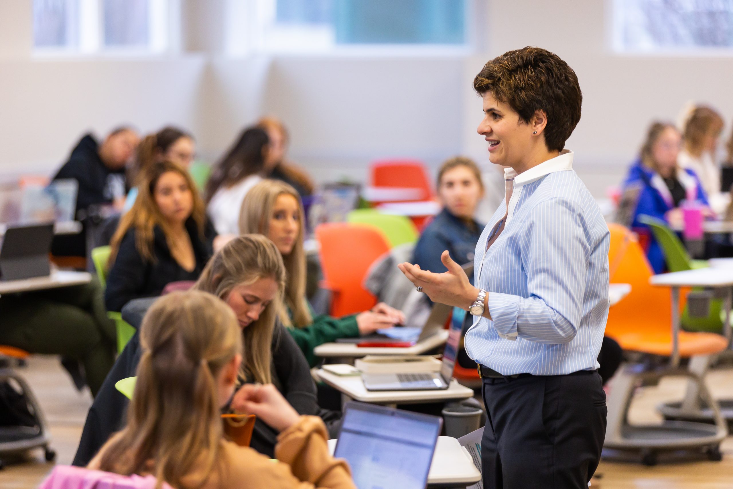 Phrosini Samis-Smith ’06 M.S., D.H.Ed., assistant dean for health professions and assistant professor of healthcare leadership at Valpo's College of Nursing and Health Professions, standing in front of and lecturing a vibrant, colorful classroom full of sitting students on campus.
