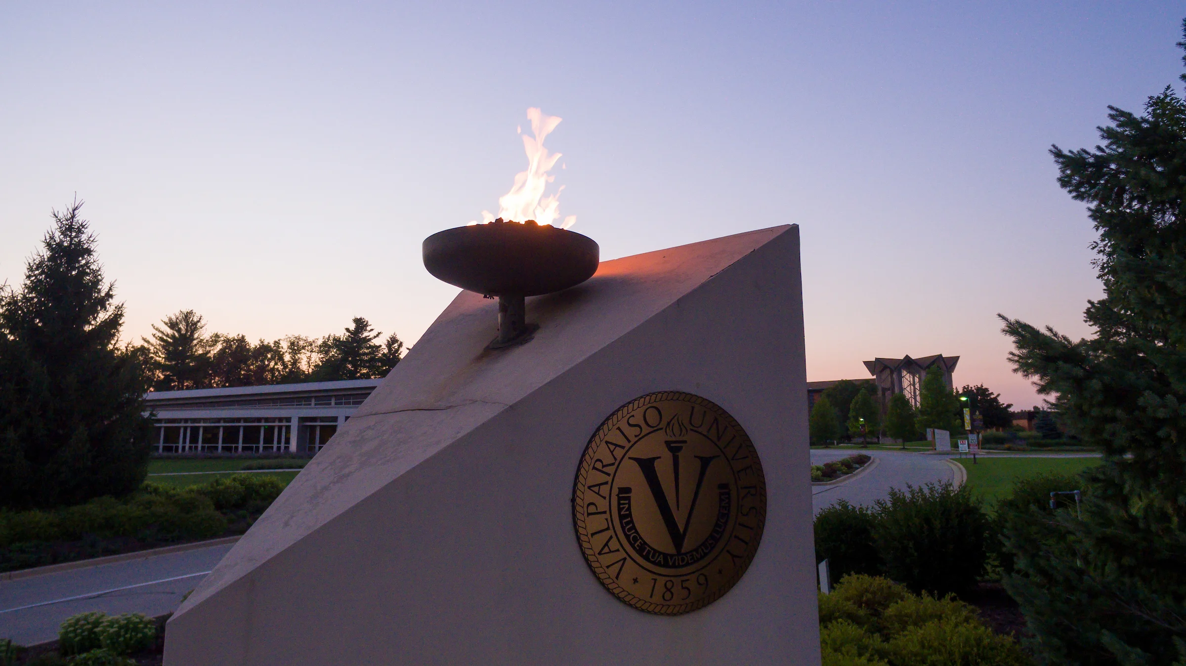 A flame burns atop a monument with the Valparaiso University seal at sunset, celebrating the impact of a $1 Million Grant from the Lilly Endowment.