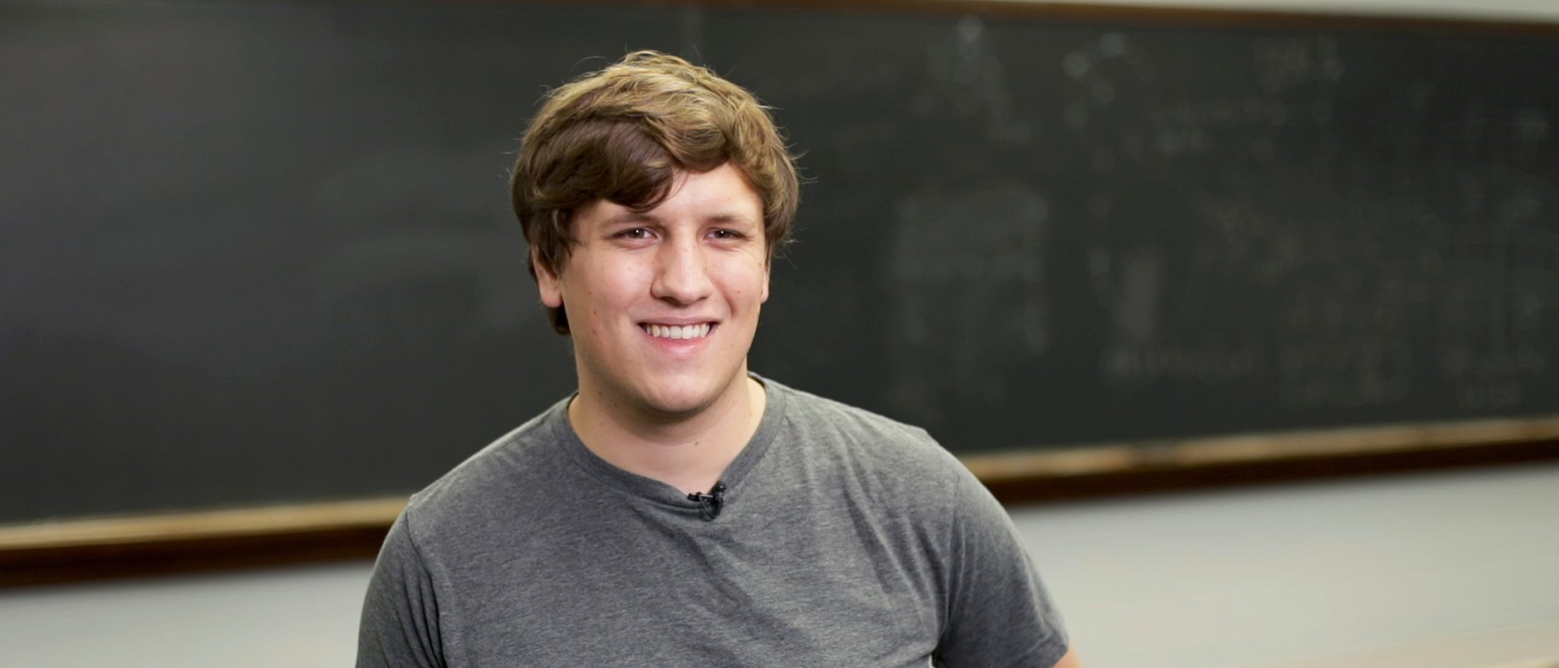 A Valpo data science student smiles in front of a blackboard in a classroom.