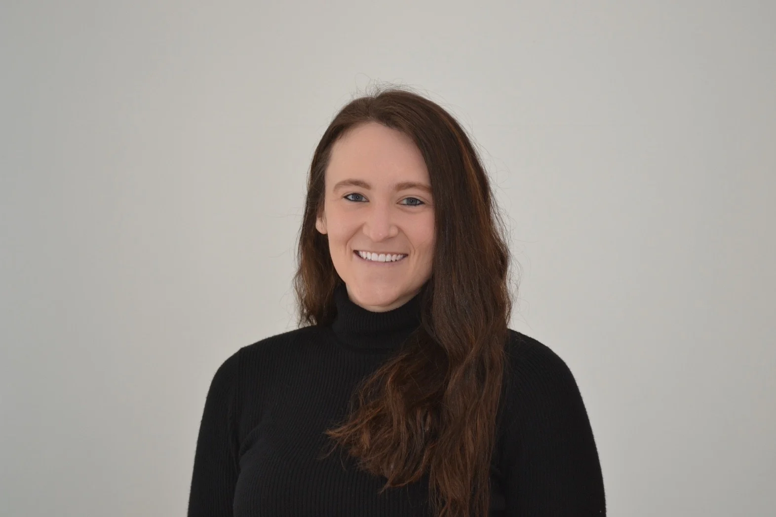 A woman with long brown hair in a black turtleneck smiles against a plain light background, radiating confidence like a beacon—this is Alexandria Lagesse.