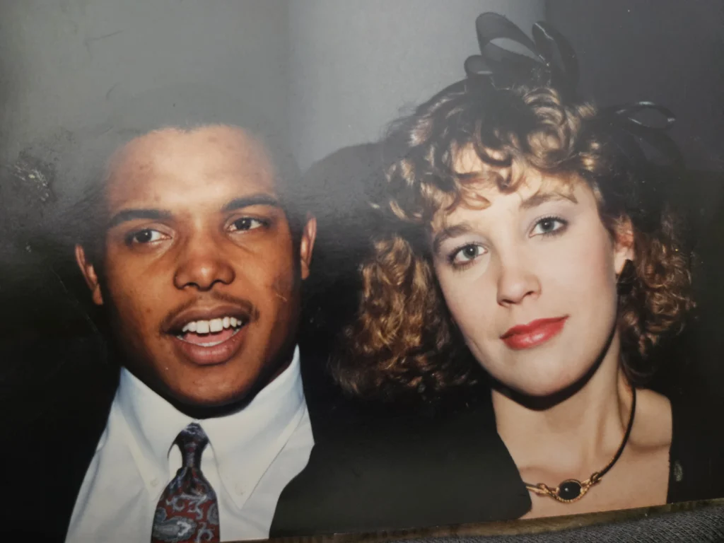 A man in a suit, Thomas Barnett, and a woman with curly hair and a black headpiece, Kim Wagner, posing together and smiling at the Beacon event.