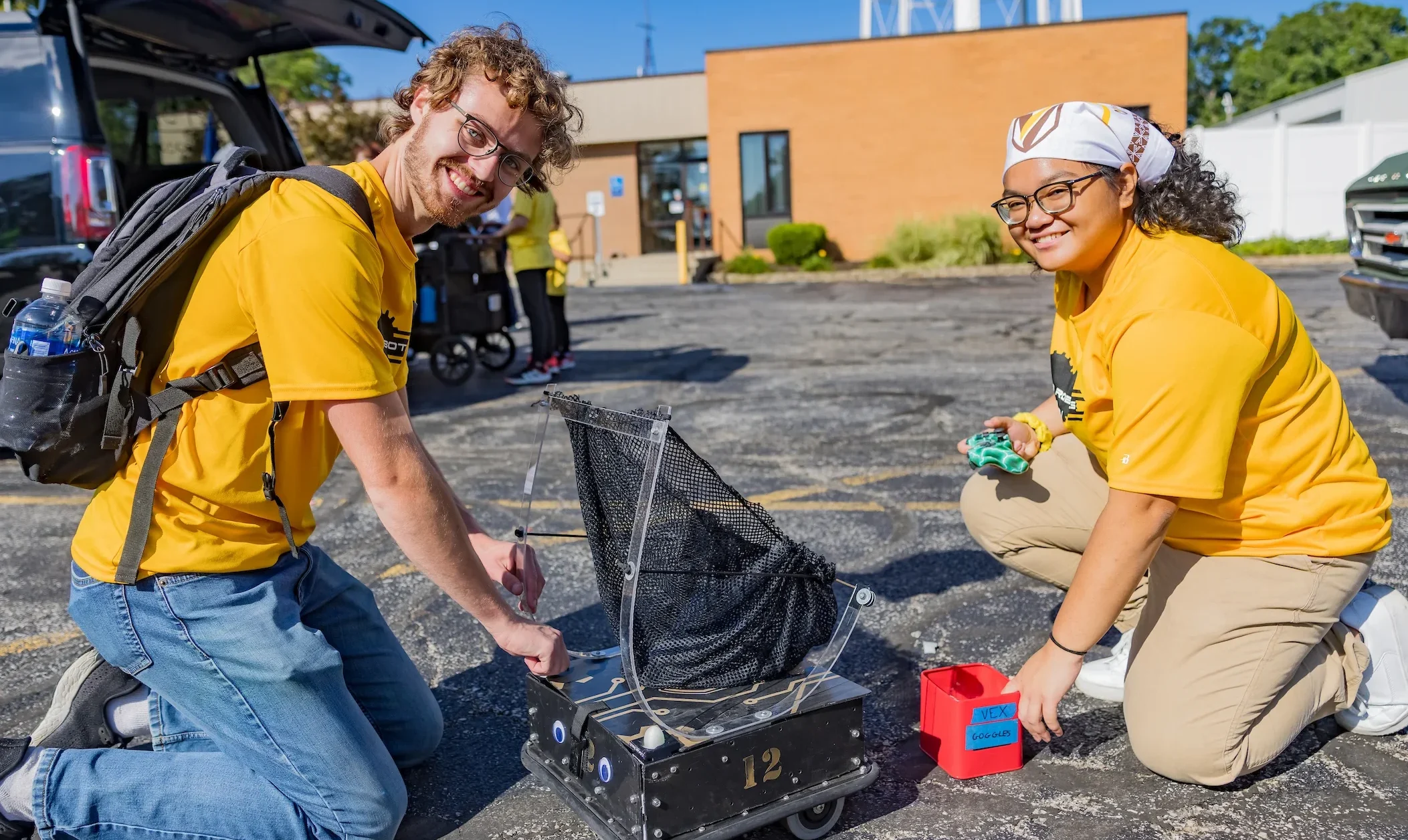 Two Valparaiso University robotics students smile while kneeling next to equipment at the local Valparaiso Popcorn Festival.