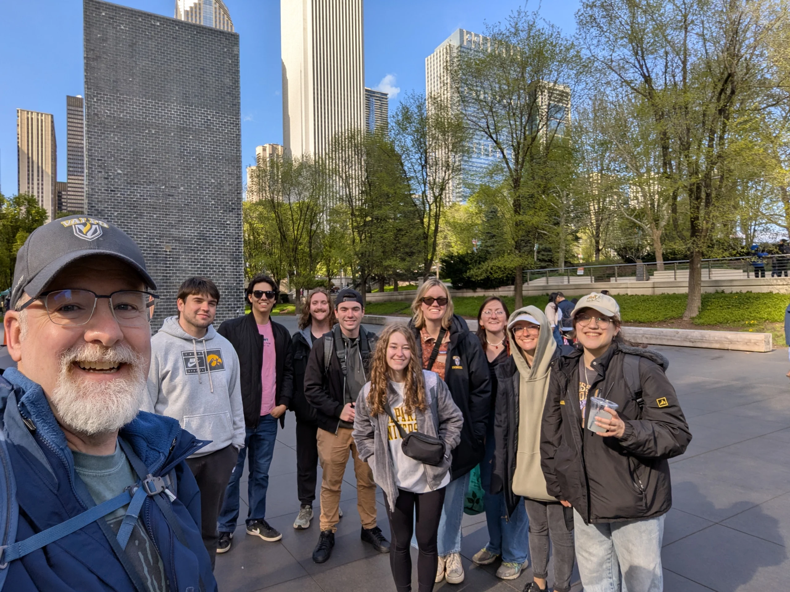 Group of people smiling outdoors in a city park with tall buildings and trees in the background, highlighting the unique geography where urban life meets nature.