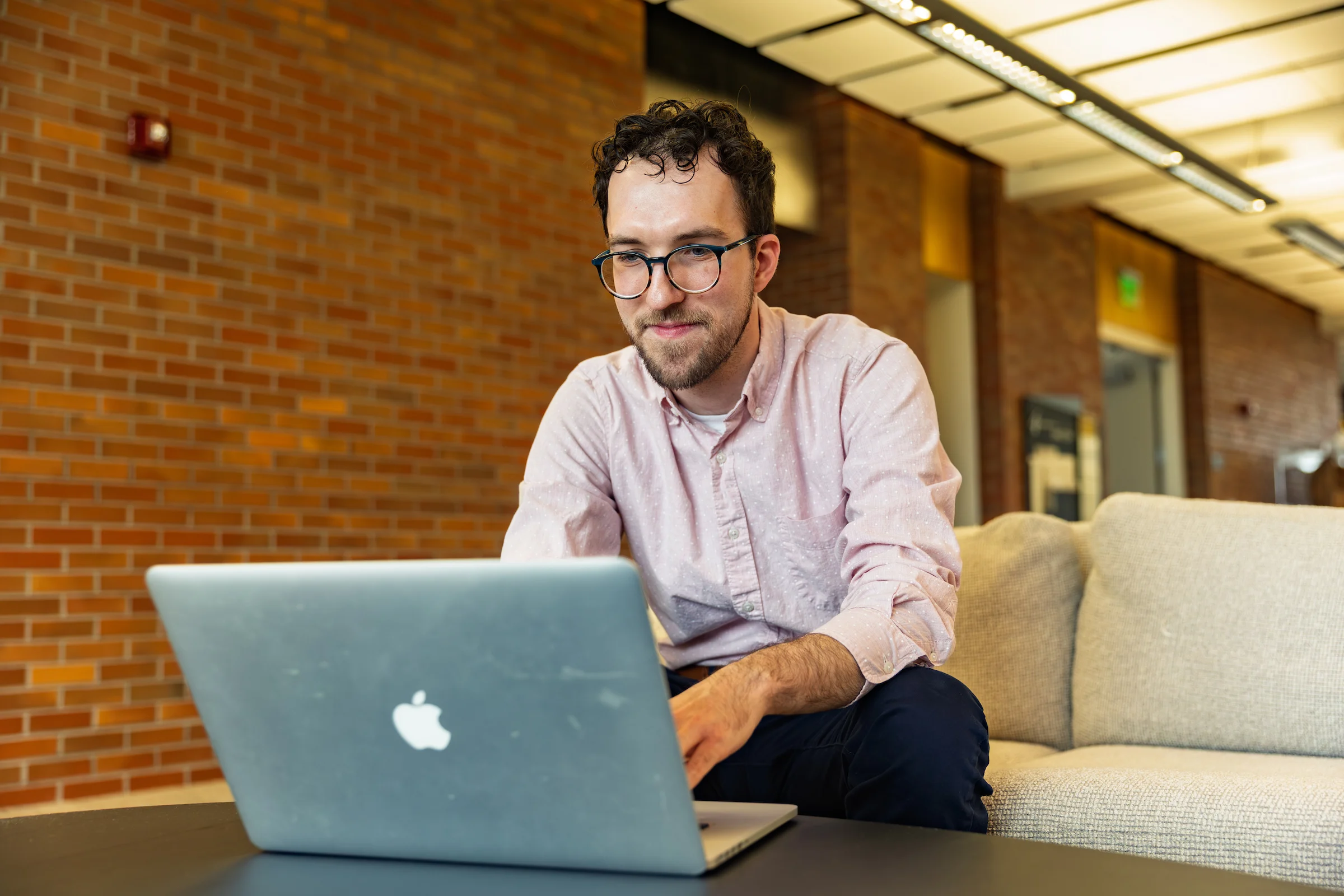 A Valparaiso University master of business administration (MBA) graduate student wearing glasses and a button-down shirt works on online coursework on a laptop.