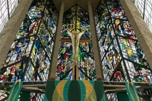 Stained glass windows and a crucifix inside a church, viewed from the front, with green cloths below, create a serene atmosphere that invites reflection on one’s calling and spiritual life.