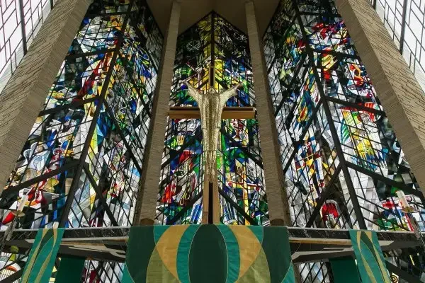 Stained glass windows and a crucifix inside a church, viewed from the front, with green cloths below, create a serene atmosphere that invites reflection on one’s calling and spiritual life.