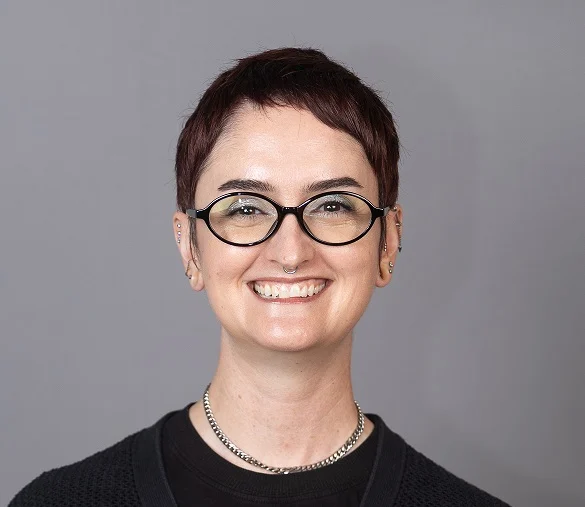 Janneal Gifford with a short haircut, glasses, and a septum piercing smiling at the camera.