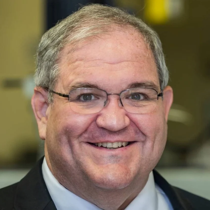 Smiling man wearing glasses, a suit, and tie, with gray hair, in an indoor setting—Doug Tougaw, P.E., Ph.D.
