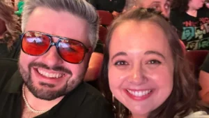 A man in sunglasses and a woman smiling, taking a selfie at a crowded indoor event—Beacon alumni celebrating together at a concert.
