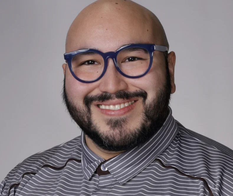 Thomas Arce, an education professional with a beard and dark-rimmed glasses, wearing a striped shirt and smiling.