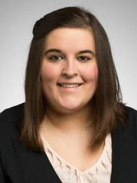 Alison Downey, a woman with straight brown hair, wearing a black cardigan and light blouse, smiles at the camera.